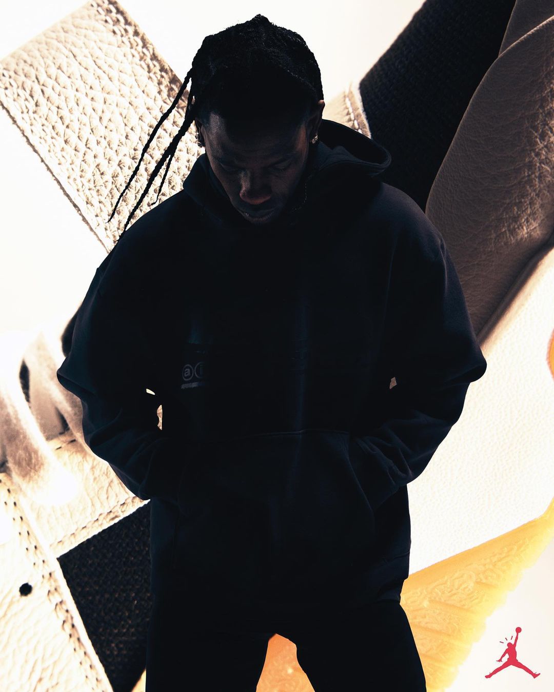 A silhouetted adult male wearing a black hoodie with the Jordan logo is set against a textured off-white background and a Jordan logo.