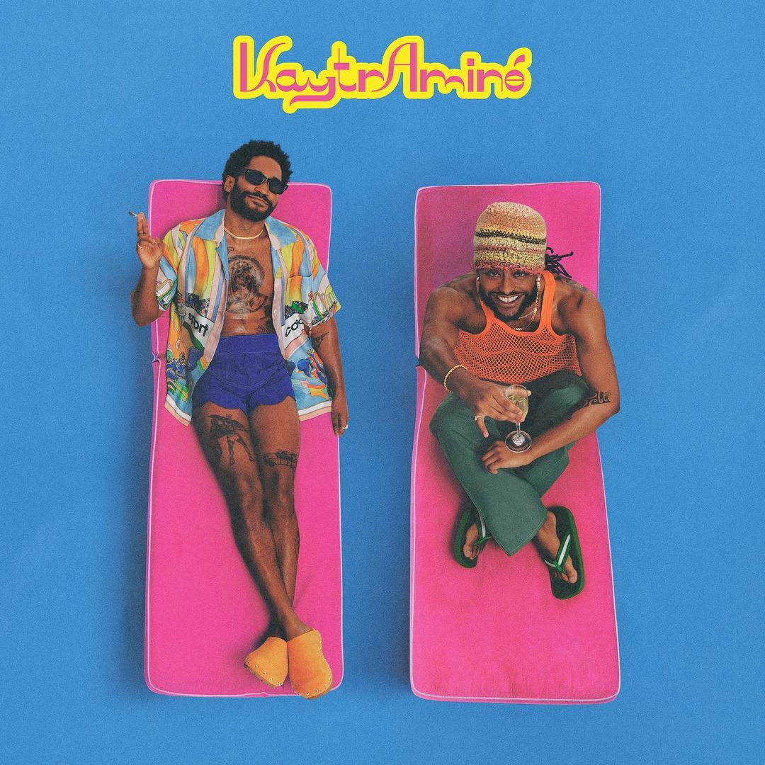 Two men lounge on pink beach mats against a blue backdrop, promoting music; one holds a glass, both sport casual summer attire.