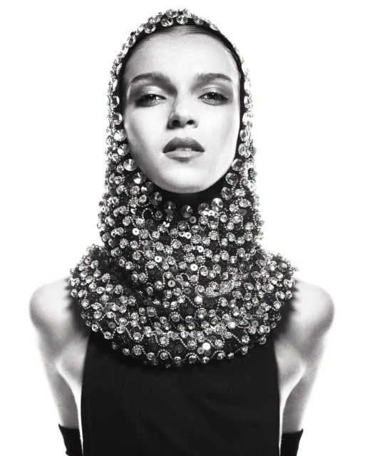 Monochrome fashion portrait of a woman wearing a beaded headpiece and sleeveless black top against a bright white backdrop in studio.