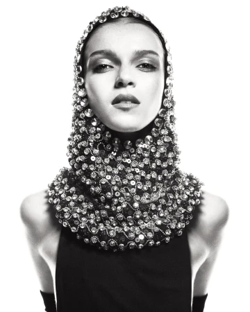 Monochrome fashion portrait of a woman wearing a beaded headpiece and sleeveless black top against a bright white backdrop in studio.