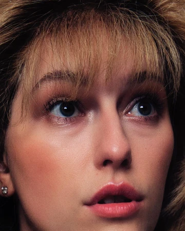 Close-up portrait of a woman with blonde hair, bangs, and blue eyes looking upward with parted lips.