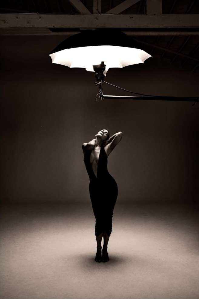Woman in black dress posing under photo studio lighting. Portrait shot with a neutral background. Fashion photography. Studio setting.
