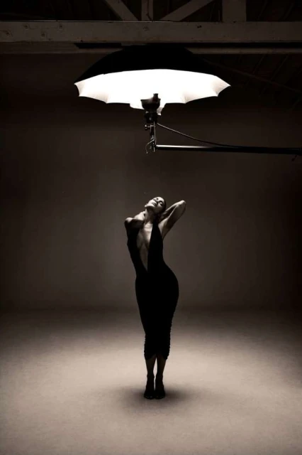 Woman in black dress posing under photo studio lighting. Portrait shot with a neutral background. Fashion photography. Studio setting.