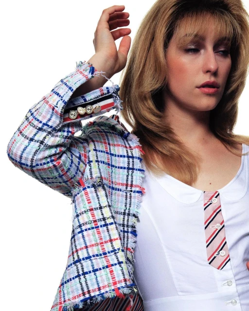 Fashion photo of a blonde woman wearing a white shirt with a decorative tie and a multicoloured plaid jacket against a white background.