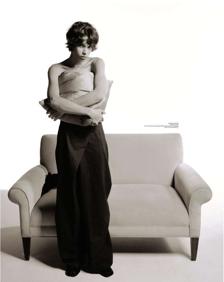 Portrait of a young adult wearing a brown wrap around the waist and holding a pillow in a photo studio setting with a couch.