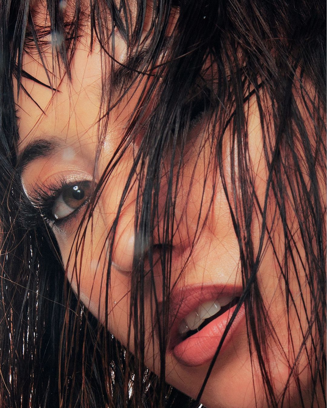 Close-up portrait of an adult woman's face with wet dark hair partially covering her face, showcasing her eye and open mouth.
