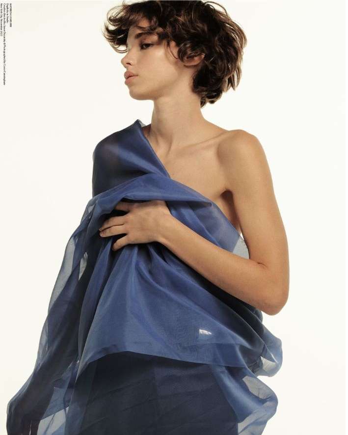 A woman with short dark curly hair wrapped in a blue translucent fabric against a white background