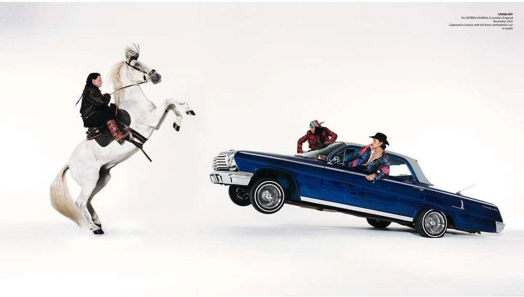 A striking photo captures two people in a lowrider car and a woman on a rearing white horse against a stark white background.