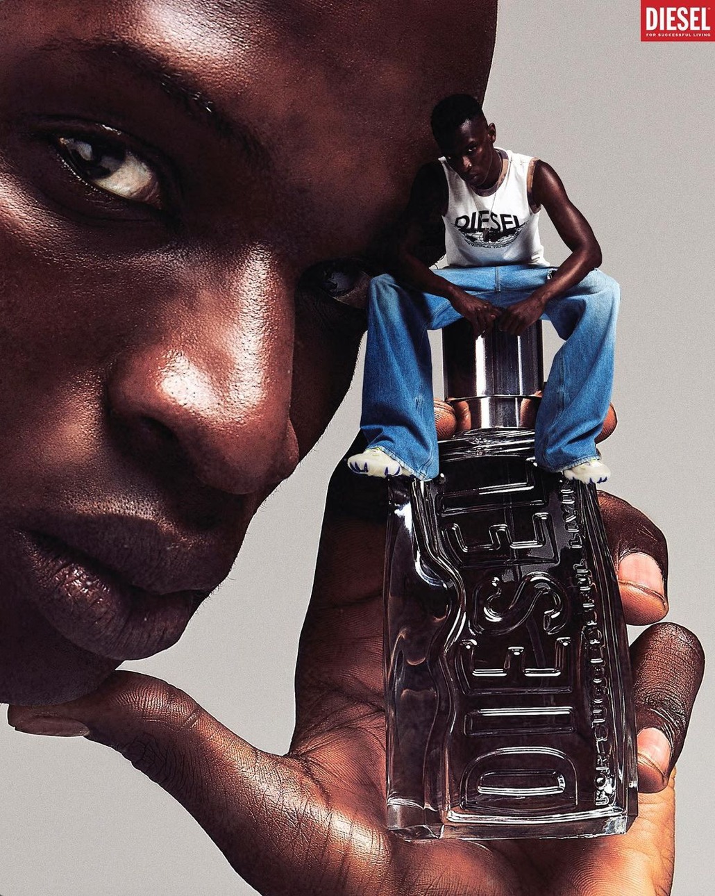 Diesel fragrance advert with a close-up of a Black male and a miniature male figure sitting atop a perfume bottle.