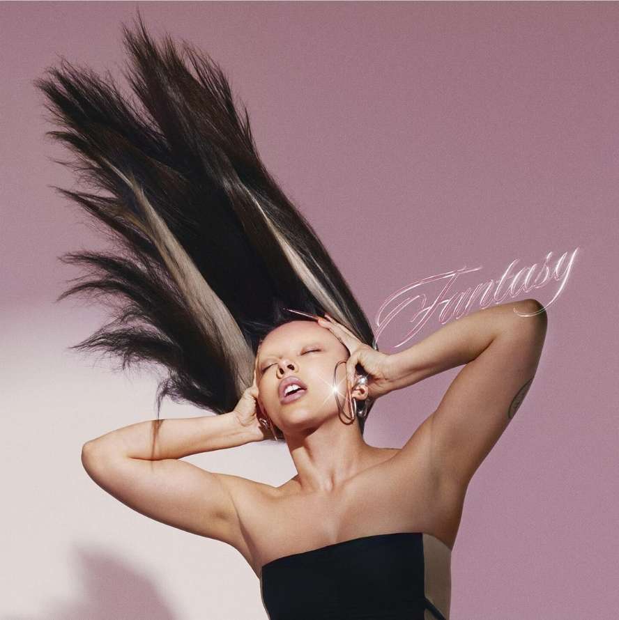 Woman in black top with dark hair tossed upward against a pink backdrop by Conor Cunningham