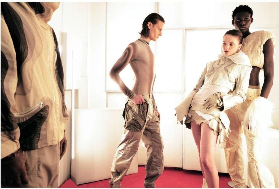 Fashion editorial shot featuring a group of diverse models in beige-toned clothing with modern, futuristic designs in a bright, indoor setting.