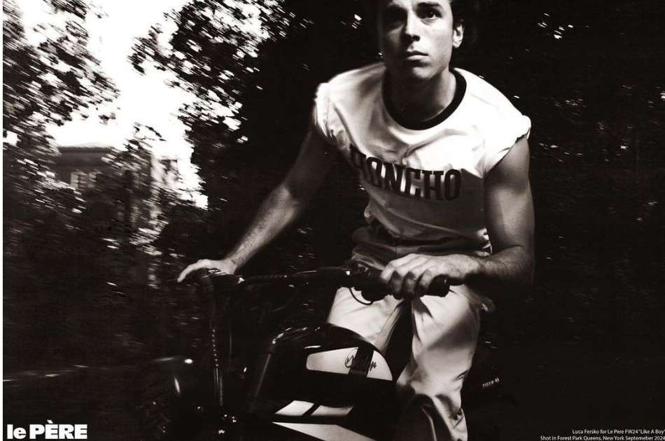 Monochromatic shot of a young adult male riding a bike outdoors on a path surrounded by trees, wearing casual athletic clothing.