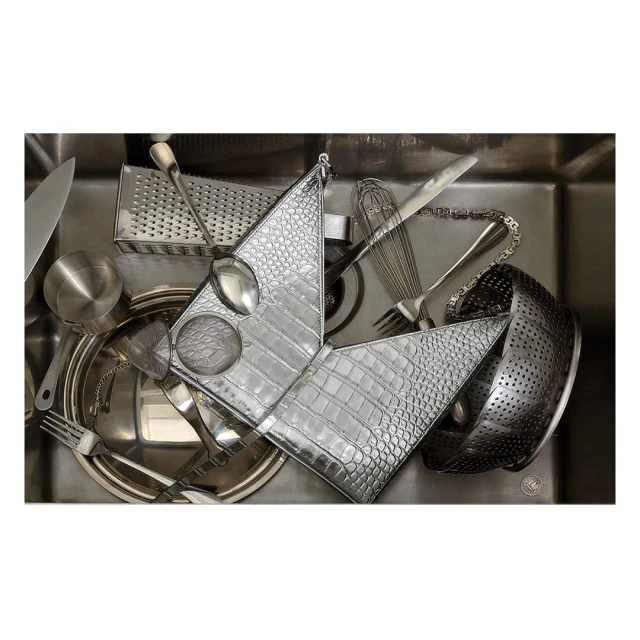 Overhead shot of a stainless steel kitchen sink filled with various kitchen utensils, including a grater, silverware, and colander.