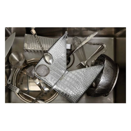 Overhead shot of a stainless steel kitchen sink filled with various kitchen utensils, including a grater, silverware, and colander.