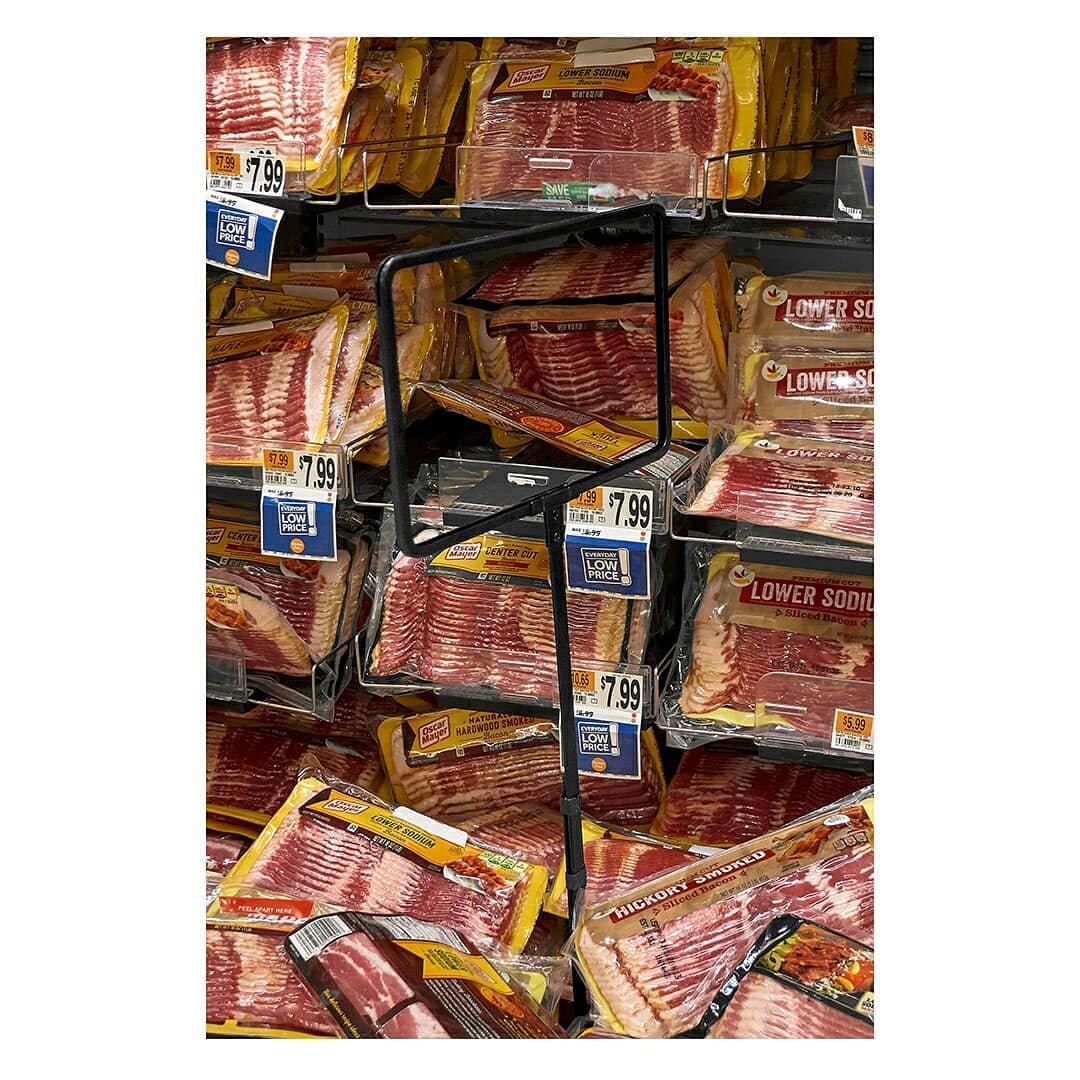 An abundance of bacon packages are stacked and displayed on metal shelves in a grocery store setting, promoting affordable low price.