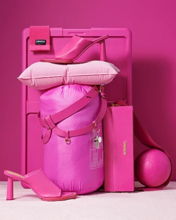 Still life arrangement of pink accessories, including high heel shoes, a tote bag, a beach towel, and a soccer ball against a pink backdrop.
