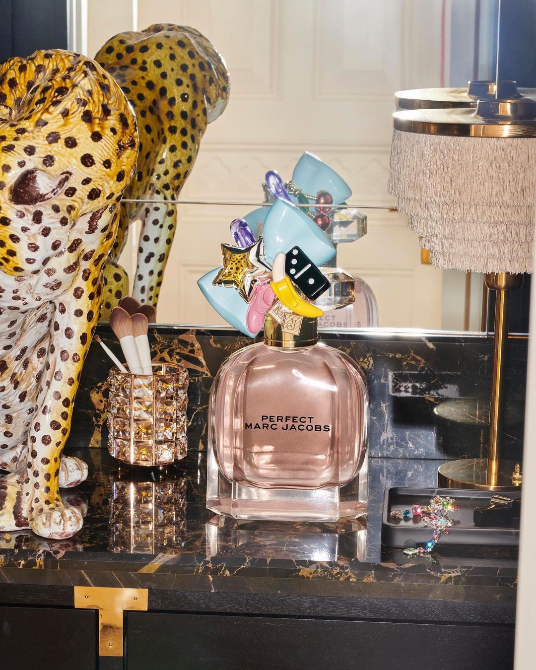 Perfume bottle of Perfect Marc Jacobs sits on a black marble-style vanity with a leopard statue and makeup brushes in the background.