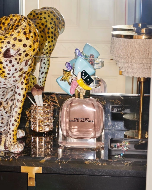 Perfume bottle of Perfect Marc Jacobs sits on a black marble-style vanity with a leopard statue and makeup brushes in the background.