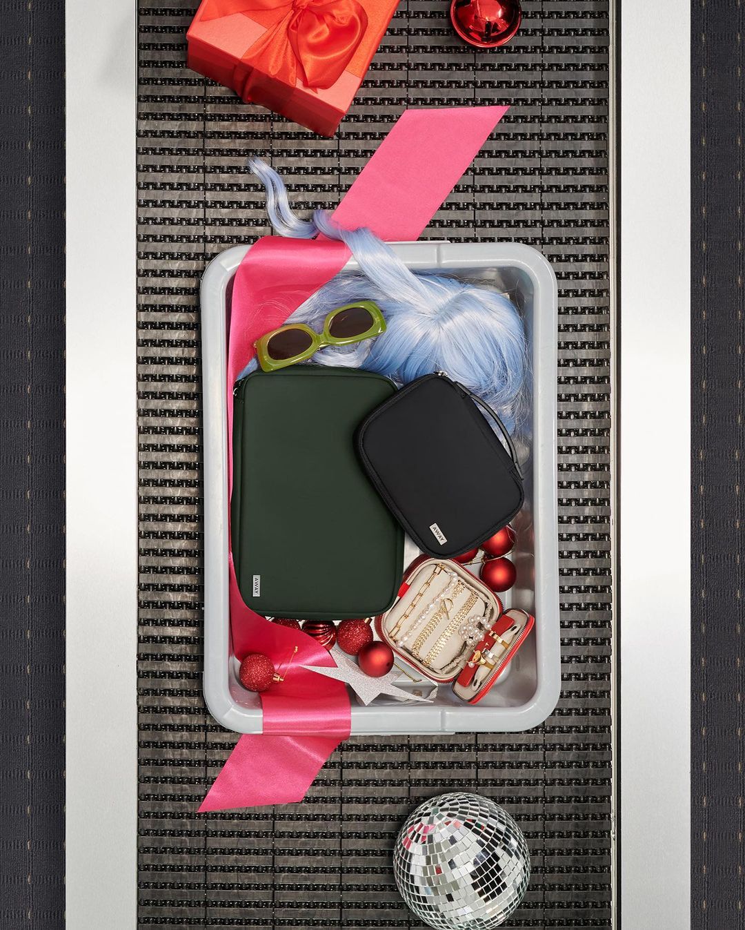 Overhead shot of a security tray filled with beauty and fashion accessories like handbags, jewelry, a wig, sunglasses, and a gift-wrapped present.