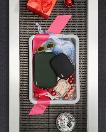 Overhead shot of a security tray filled with beauty and fashion accessories like handbags, jewelry, a wig, sunglasses, and a gift-wrapped present.