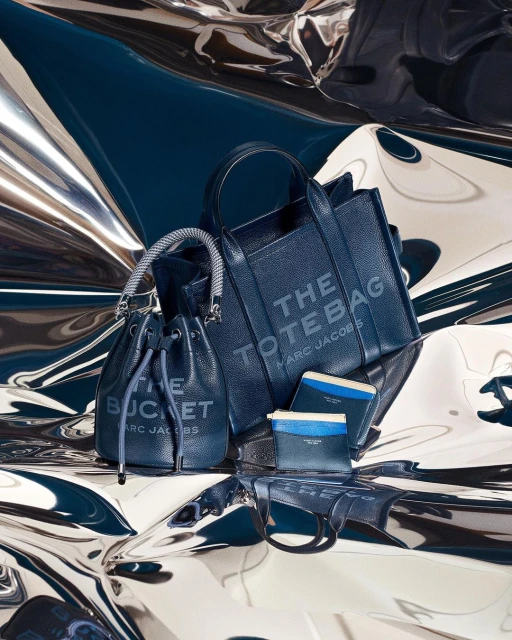 Stylish navy-blue leather handbags and cardholders arranged on a shiny silver surface, capturing a sense of modern luxury and minimalist fashion.