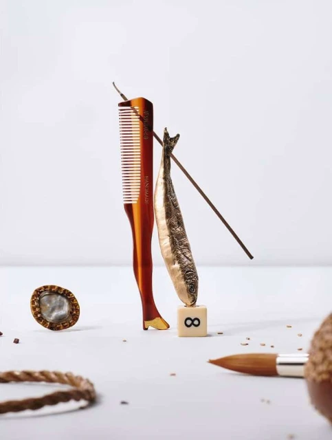 Abstract still life composition: comb with leg detail, fish, tile with '8', brush, rope circle, and small dots on a white background.
