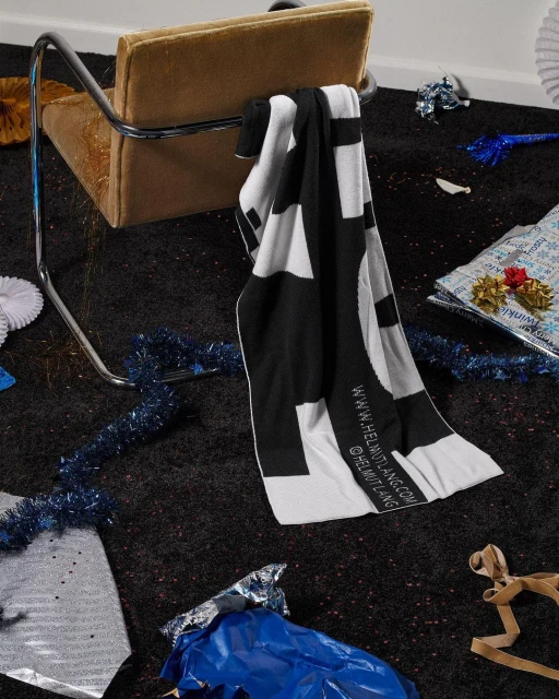 An up-close shot of a modern tan chair with metal legs, a black and white towel draped over it, and party decorations on a dark carpet.