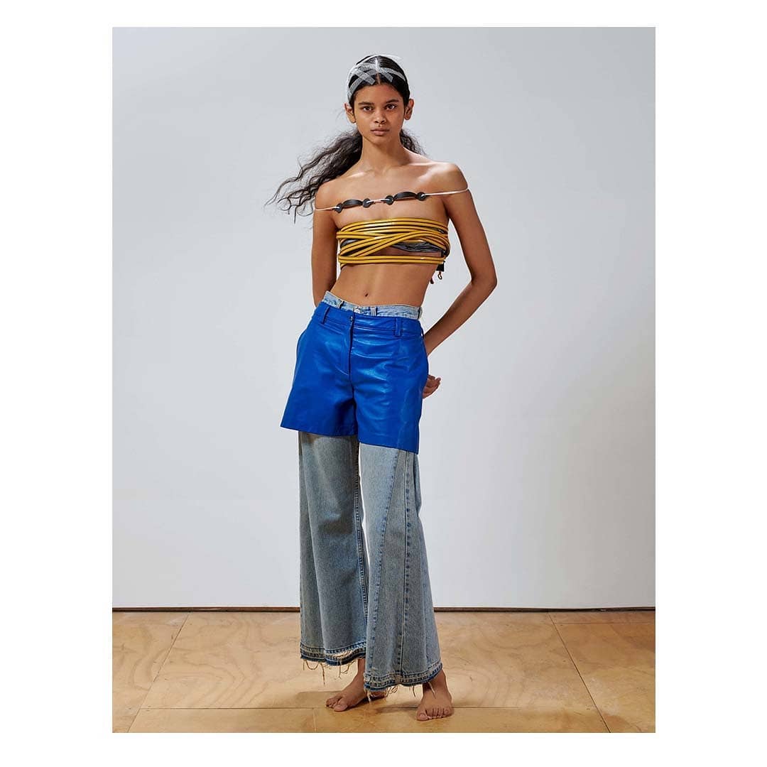 Fashion model poses in modern apparel featuring a woven top, two-tone pants, and a white background in a studio setting.