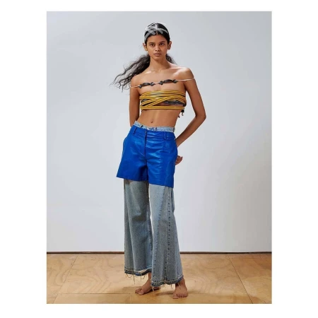 Fashion model poses in modern apparel featuring a woven top, two-tone pants, and a white background in a studio setting.