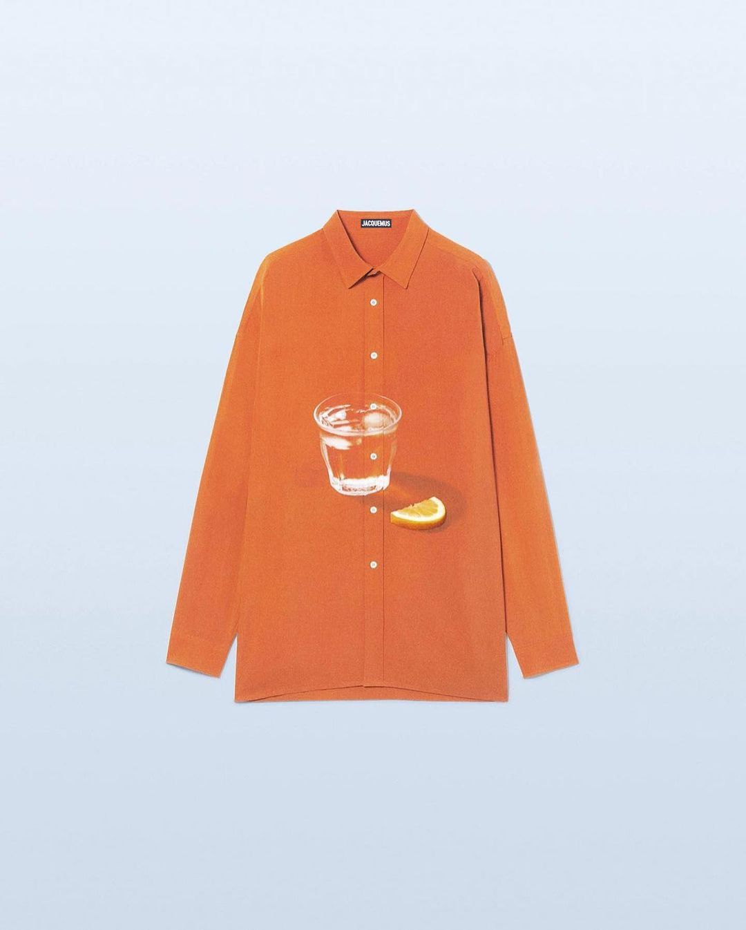 Still life: an orange button-down shirt with a glass of water and a slice of citrus fruit against a light blue backdrop.