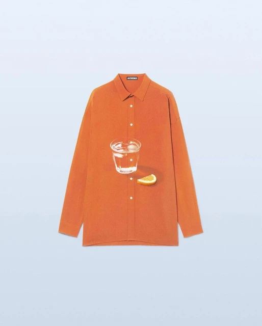 Still life: an orange button-down shirt with a glass of water and a slice of citrus fruit against a light blue backdrop.