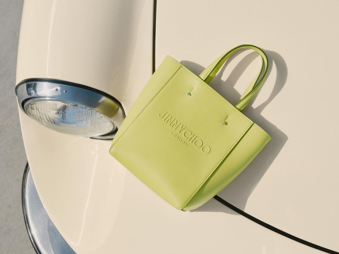 Lime green Jimmy Choo tote bag displayed on a vintage car hood, emphasizing fashion and classic automotive design.