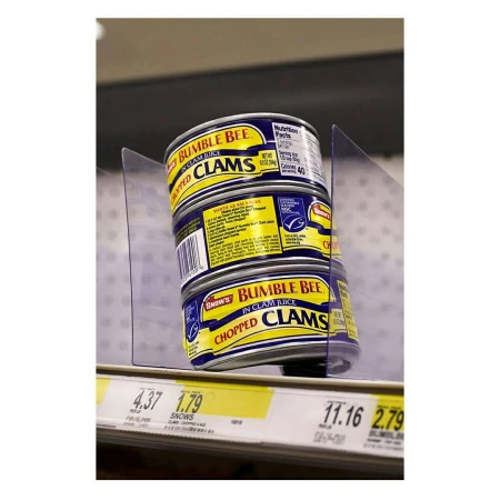 Stack of Bumble Bee brand canned clams on a grocery store shelf with visible pricing tags. The canned goods are brightly lit.