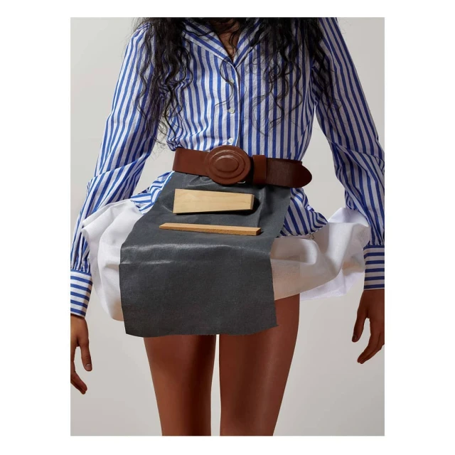 Fashion shot featuring a woman wearing a striped shirt, brown belt, white skirt, and wooden objects against a neutral background.