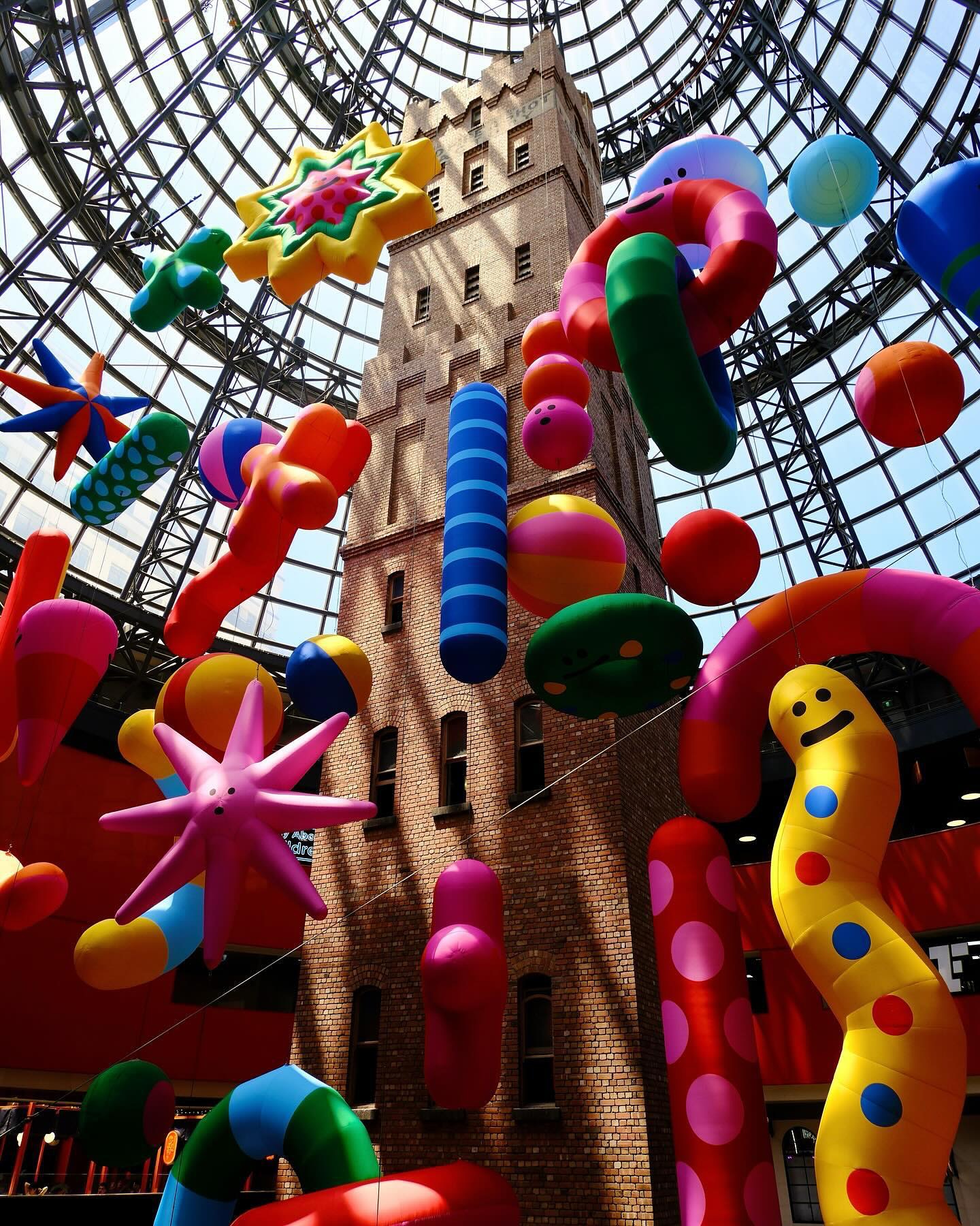 Interior view of the Royal Arcade in Melbourne, Australia featuring a tall brick structure surrounded by colorful inflatable decorations.