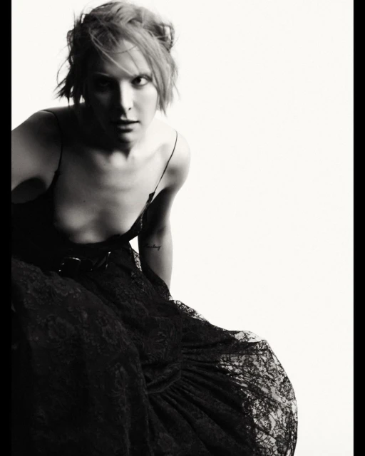 Black-and-white portrait of a woman in a black dress with a lace skirt, looking at the camera against a bright white background.