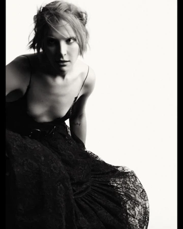 Black-and-white portrait of a woman in a black dress with a lace skirt, looking at the camera against a bright white background.