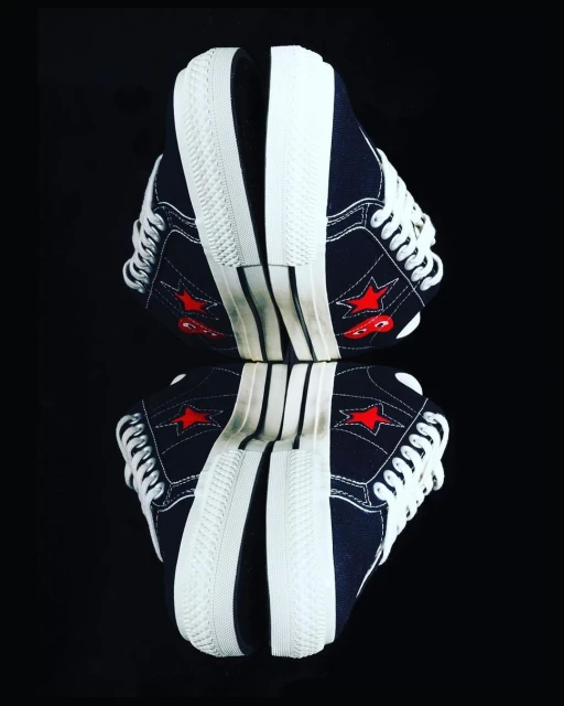 Two blue canvas sneakers with white soles and laces face each other, mirrored on a black reflective surface with a shallow depth of field.