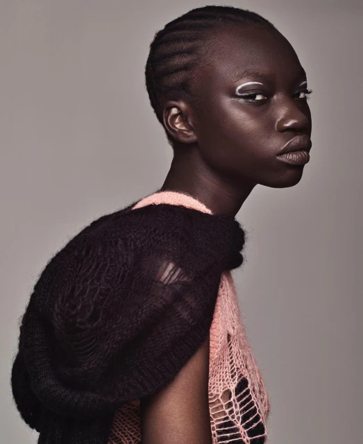 Close-up of a young African American woman with braided hair, wearing a knitted top with an open weave, and striking white eyeliner.