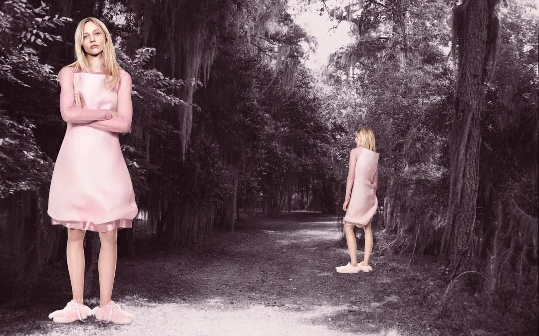 Two fair-skinned adult females wearing pink dresses and sneakers in a forest with a path, captured with a medium shot and natural light.