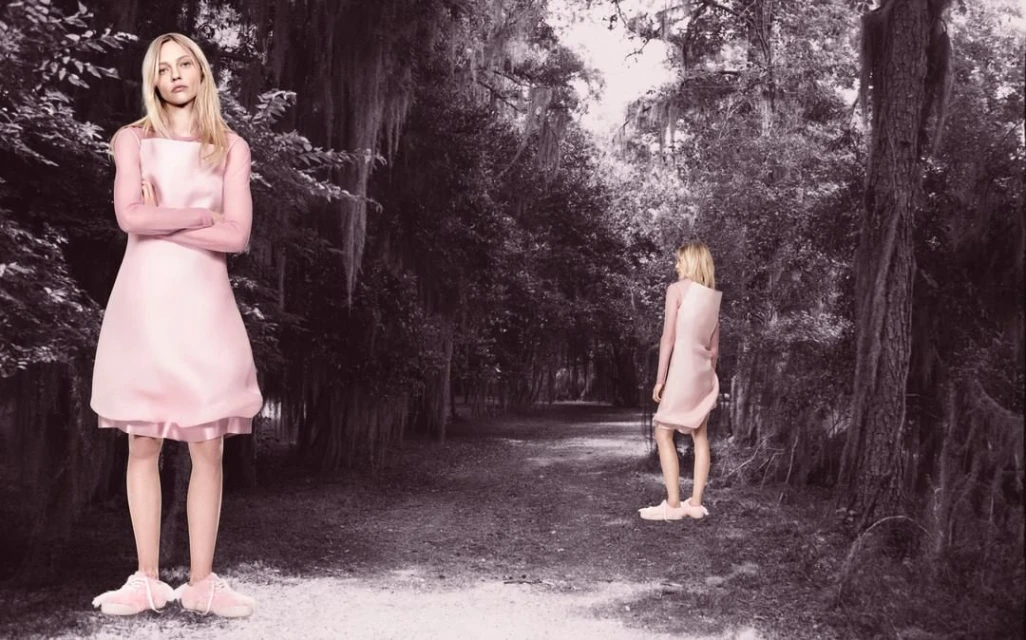 Two fair-skinned adult females wearing pink dresses and sneakers in a forest with a path, captured with a medium shot and natural light.