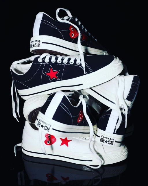 Stack of Converse One Star sneakers featuring a red star emblem and a red heart-and-eyes logo, set against a dark background.