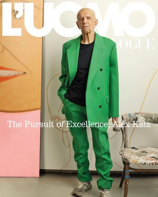 Magazine cover of an older adult male in a green suit, posing next to an abstract painting and a chair in an indoor setting.