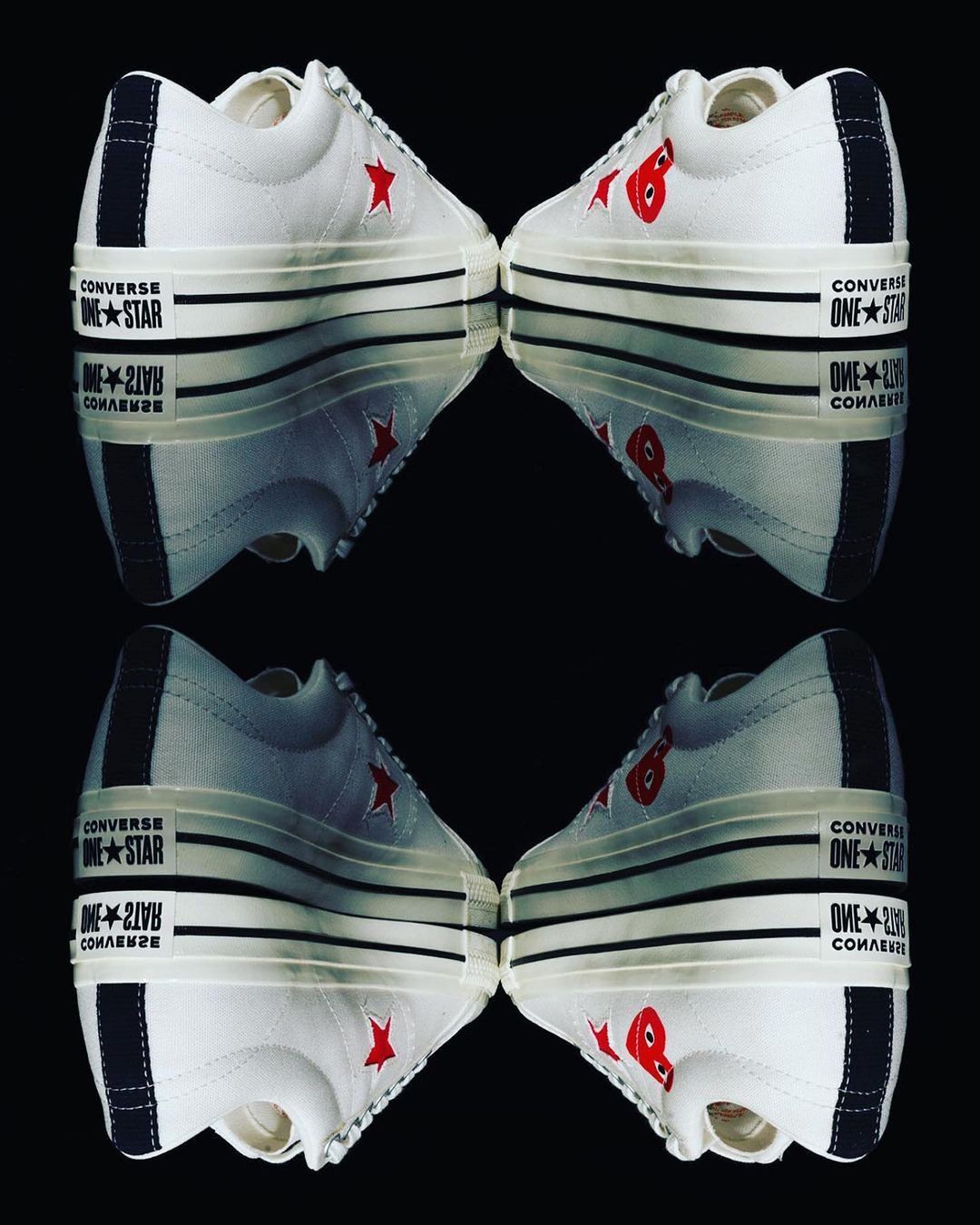 Two pairs of Converse One Star Comme des Garçons sneakers mirrored against a black background, showcasing their unique design.