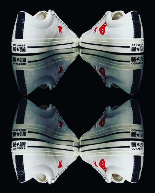 Two pairs of Converse One Star Comme des Garçons sneakers mirrored against a black background, showcasing their unique design.