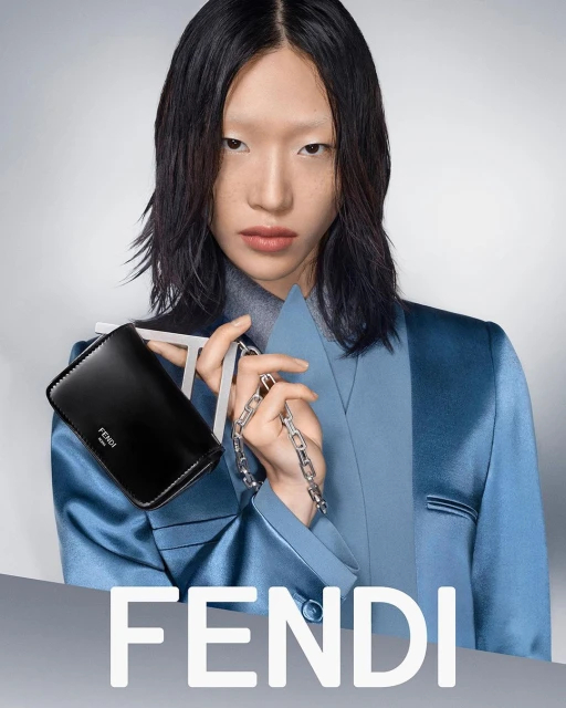Asian model presents a black Fendi purse with a silver chain against a gradient grey backdrop in a studio fashion shot.