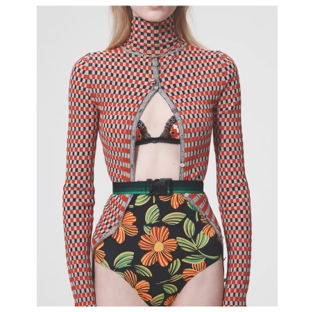 Model wearing a checkerboard turtleneck top and floral patterned briefs with a green belt against a white background