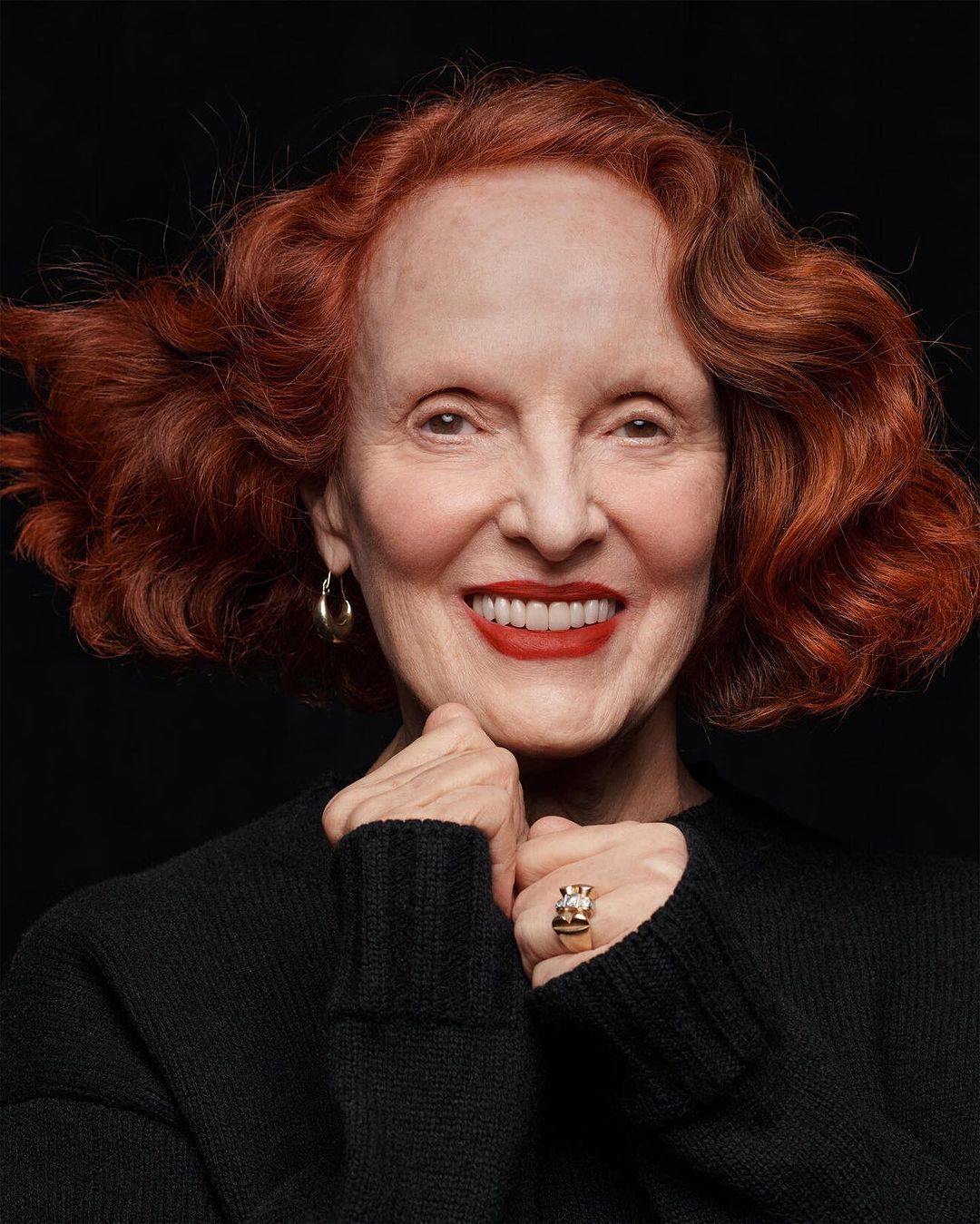 Portrait of an elderly woman with red hair wearing a black sweater against a dark background by Craig McDean