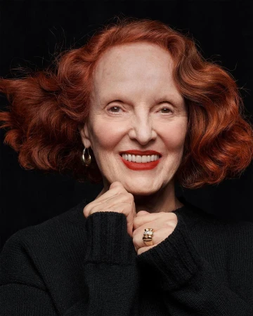Portrait of an elderly woman with red hair wearing a black sweater against a dark background by Craig McDean