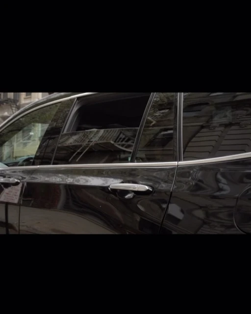 Side view of a shiny black SUV parked outdoors, reflecting the surroundings in its windows. The vehicle is parked on a street.